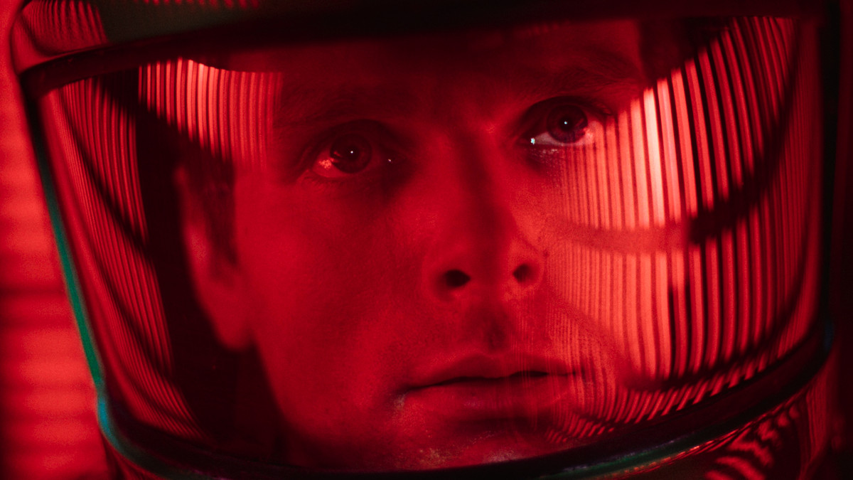 A man in a space helmet stares up at rows of red illuminated columns of light.