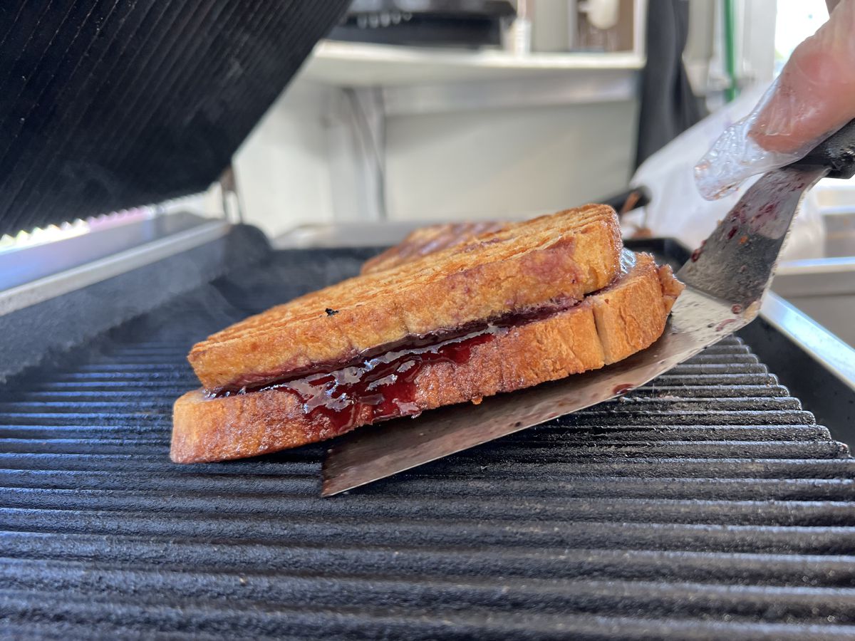 A strawberry jam sandwich on a spatula on a grill. 