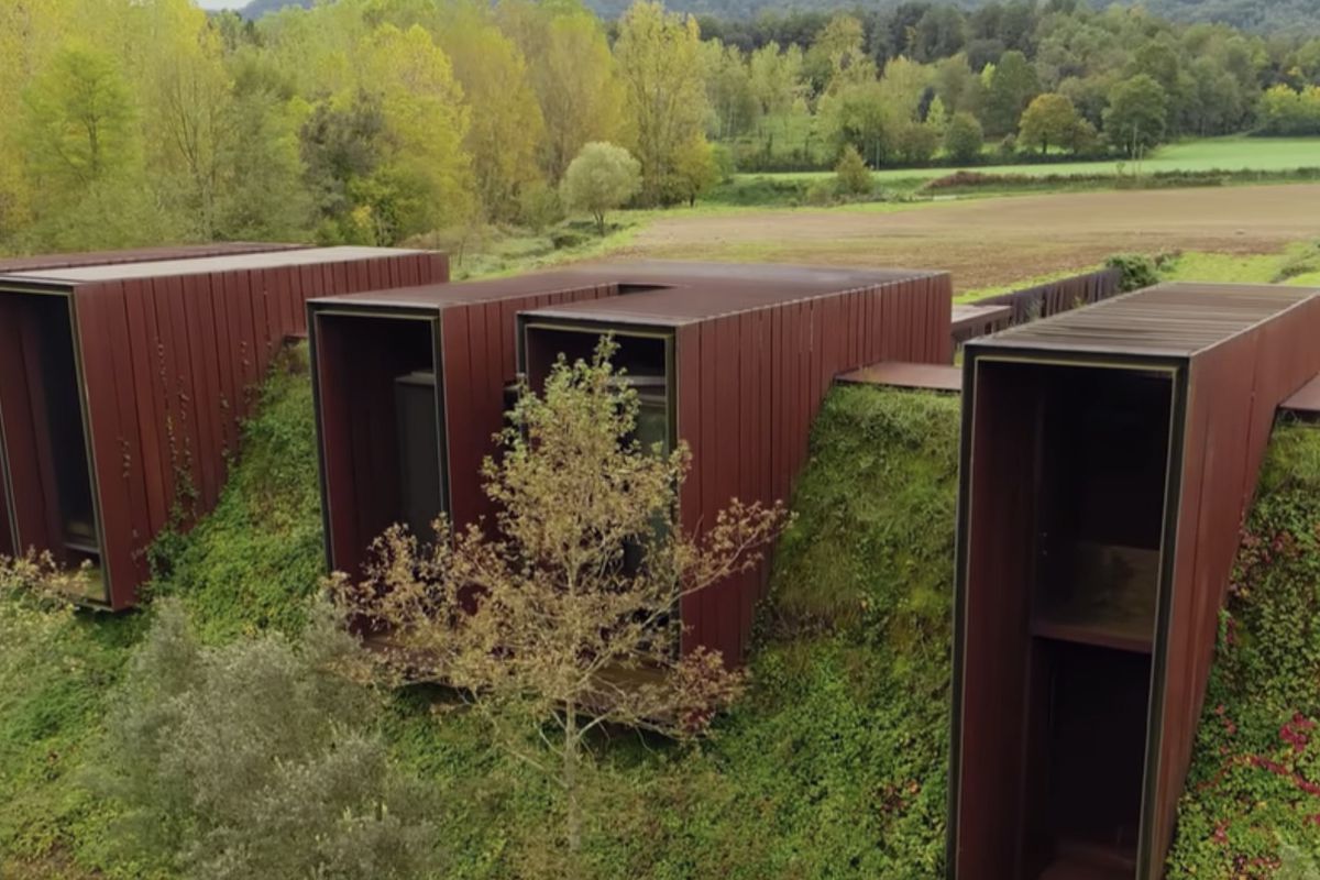A bermed house built into a green hill features five agrarian-inspired boxes meant to look like farm sheds.
