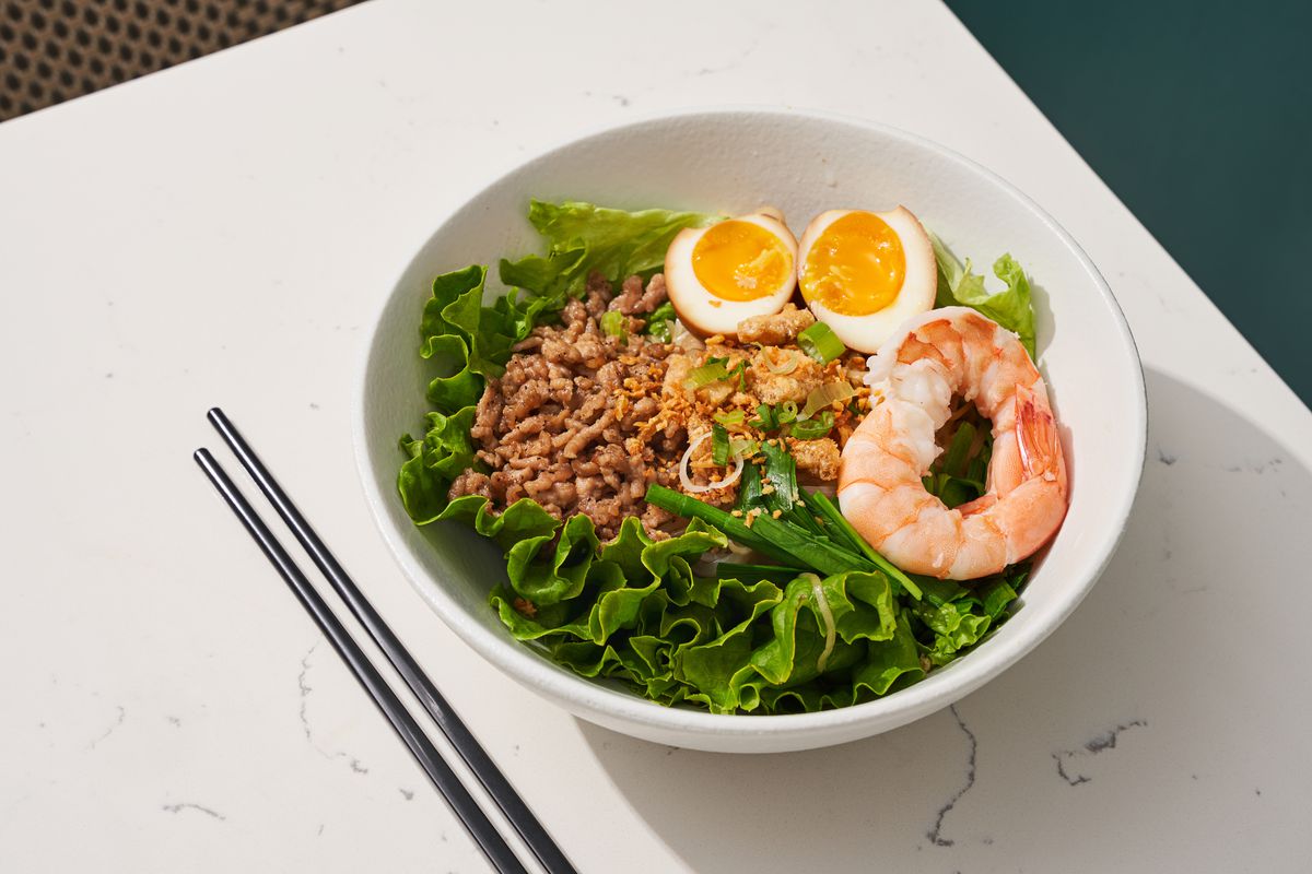 A bowl of ground beef, with two halves of a soft-boiled egg and shrimp over a bed of lettuce