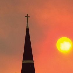 A bird soars past the steeple of the Sacred Heart Cathedral in Pueblo Colo. on June 19, 2013 as the sun shines through the smoke-filled sky darkened by smoke from several wildfires in southern Colorado this week.  