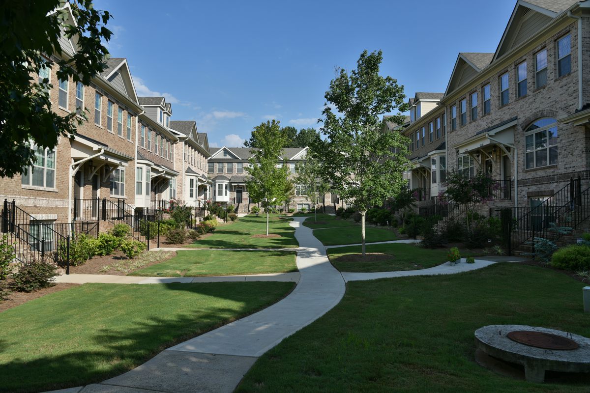 Two rows of townhomes on either side of a green space with a sidewalk in the middle. 