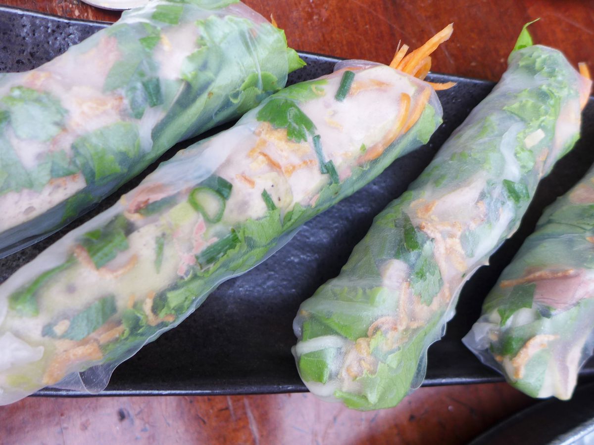 Four long semi transparent rice paper wrapper filled with cilantro and other semi-visible ingredients, angled in the frame.