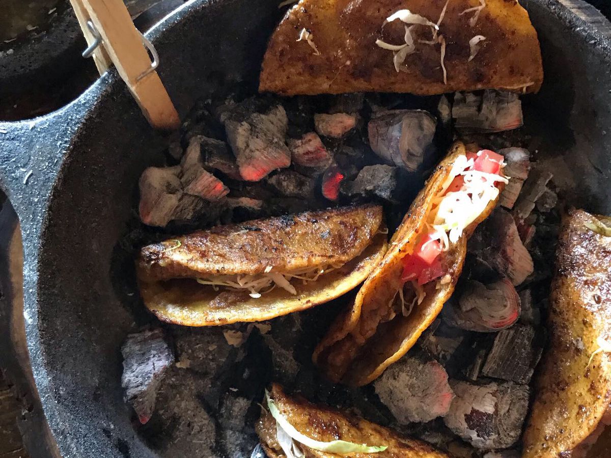 From above, five crisp tortillas folded around meat and vegetables sit in a stone bowl with hot coals