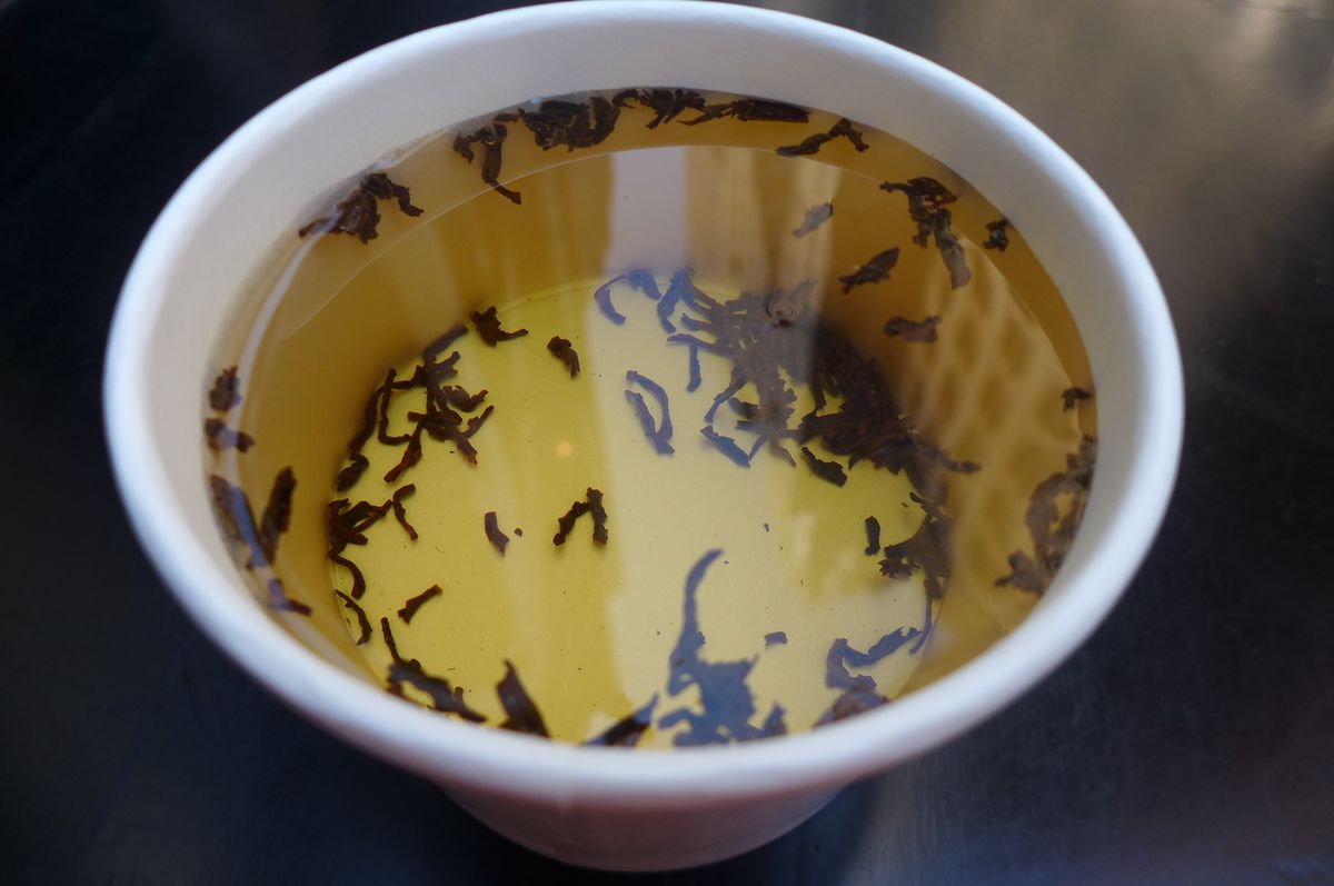 A paper cup seen from above with tea leaves floating around.