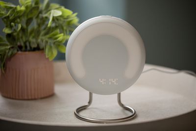 Close up of Amazon Halo Rise on a nightstand, showing circular shape, metal legs, and curved light source.