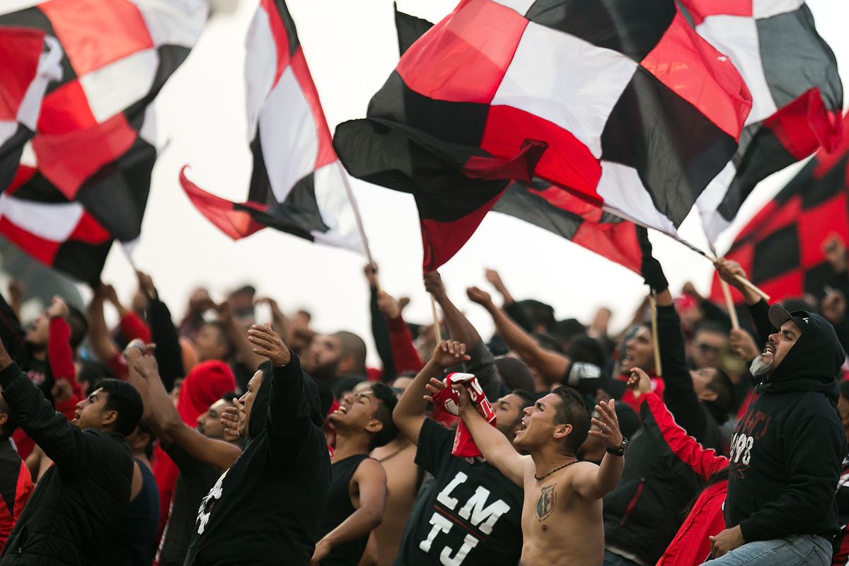 Members of La Masakr3 sing and wave flags during a Club Tijuana match.