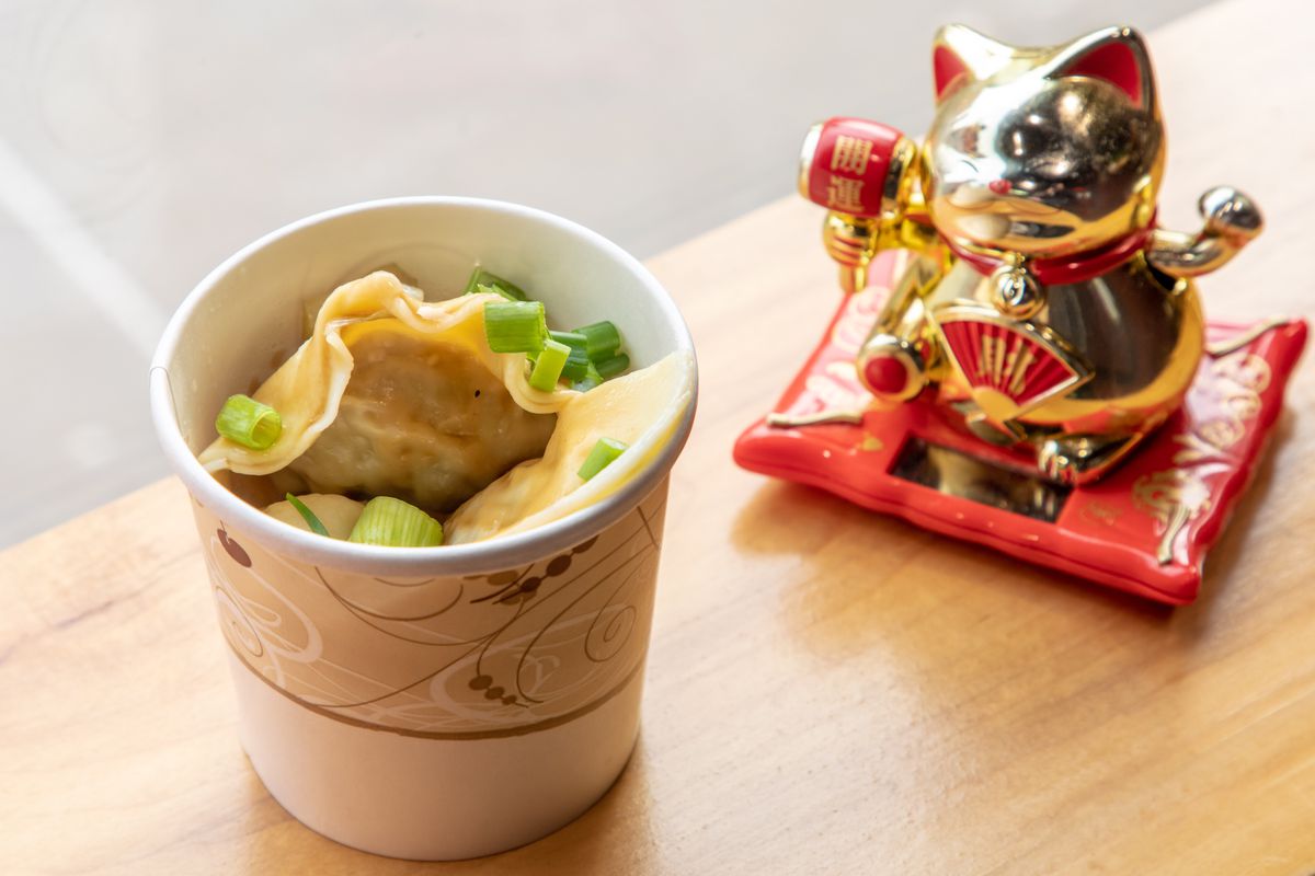 Big dumplings with scallions on top sit in a cardboard container, next to a golden lucky cat.