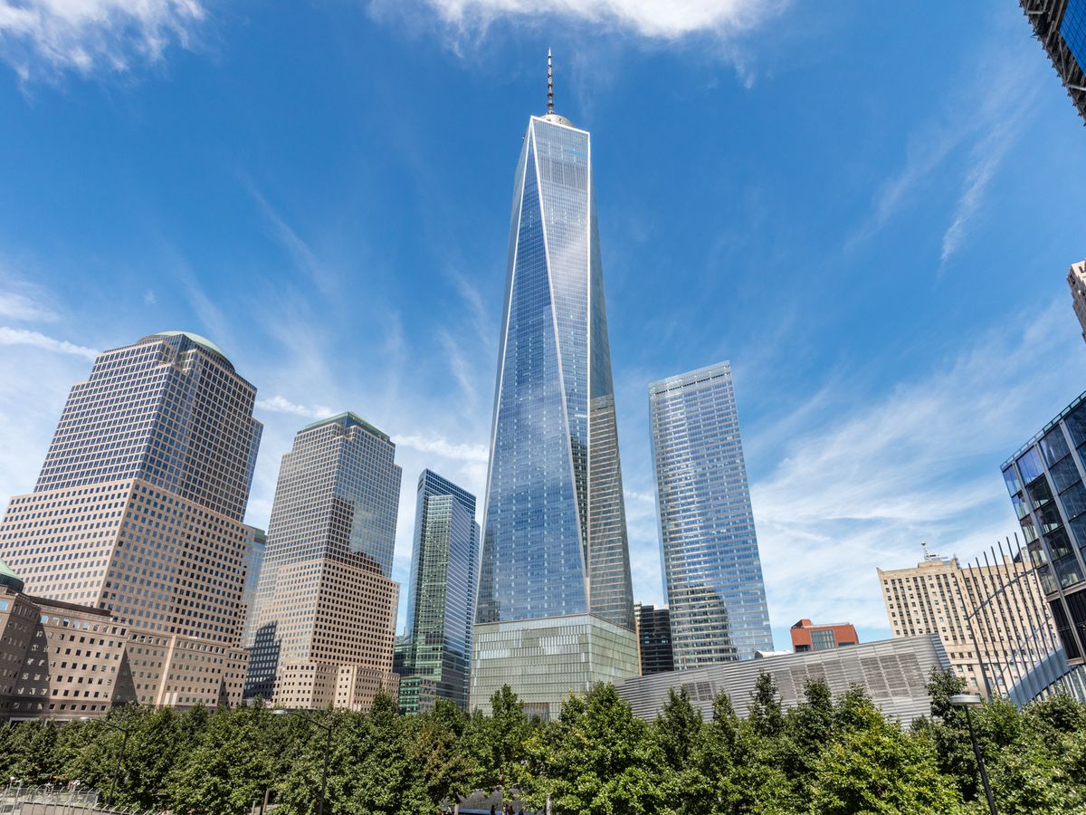Large skyscrapers including One World Trade Center. In the foreground there is a row of trees.