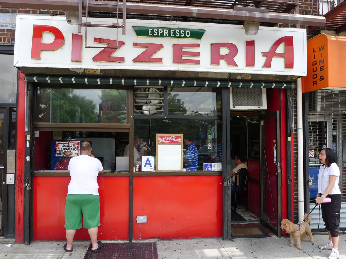 Orange pizzeria storefront with customers visible through window and open door, and a guy standing outside a pizza window, as a woman with a furry dog looks on and yawns.