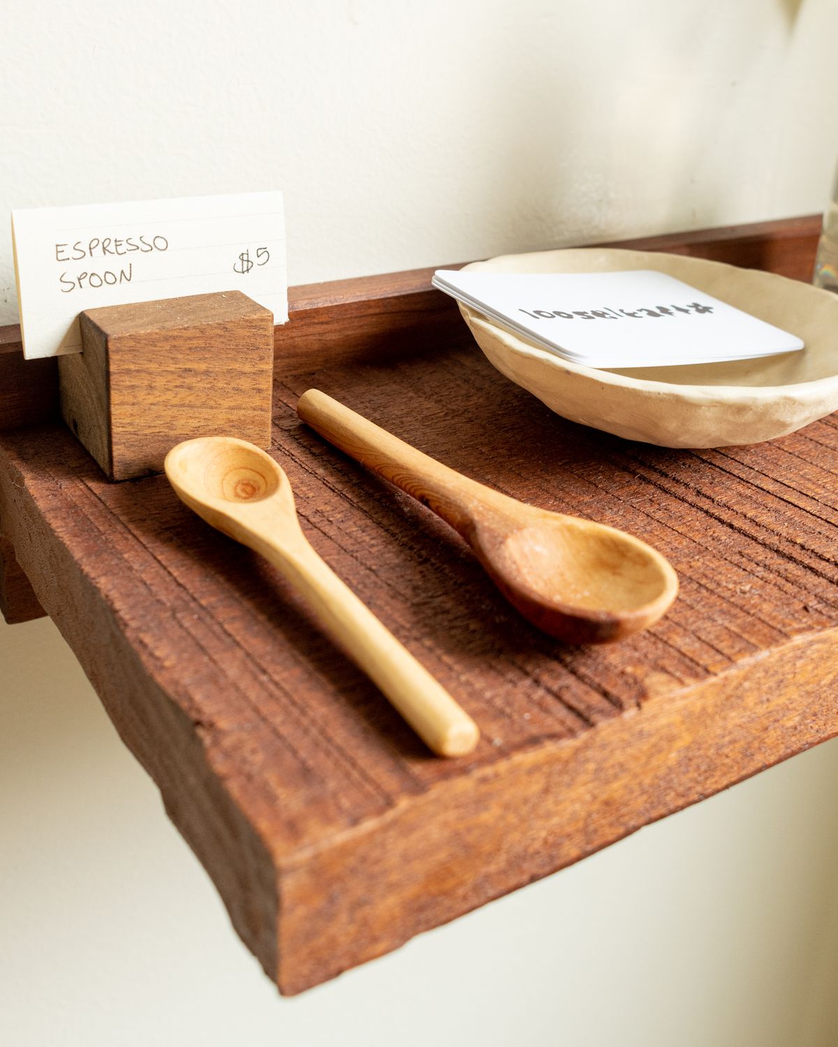 A wooden shelf holds carved wooden espresso spoons and a small ceramic dish.