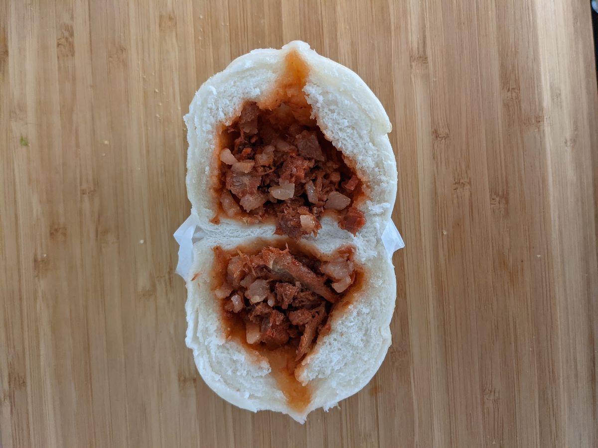 A cross section of a steamed char siu bao (Chinese BBQ pork bun). White, fluffy bread is filled with reddish BBQ pork.