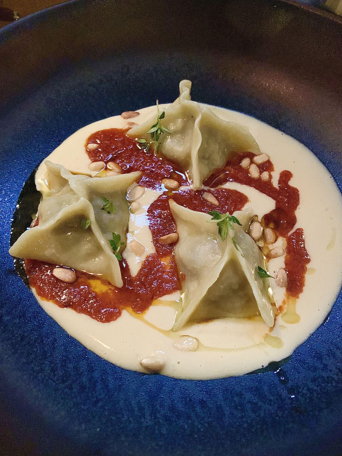 Beef and sour cherry manti dumplings, in a pool of yoghurt with a zig-zag of tomato and chilli butter, in a blue bowl