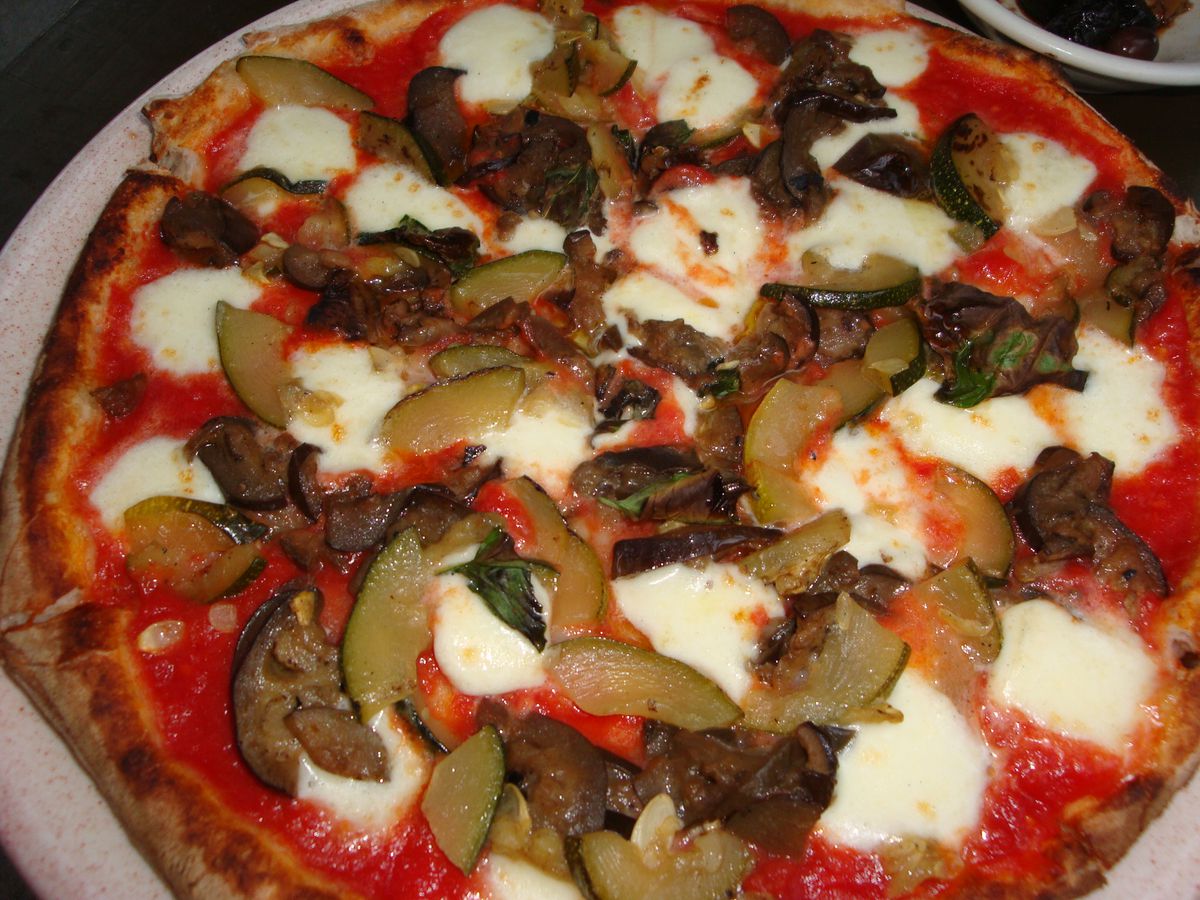 A pizza with squash, eggplant, tomato sauce, and splotches of cheese.