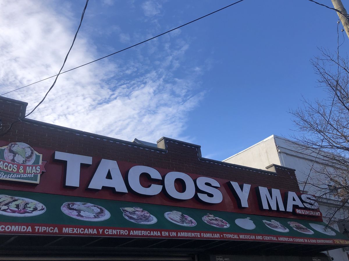 An exterior sign with white lettering spelling out Tacos Y Mas against a red background.