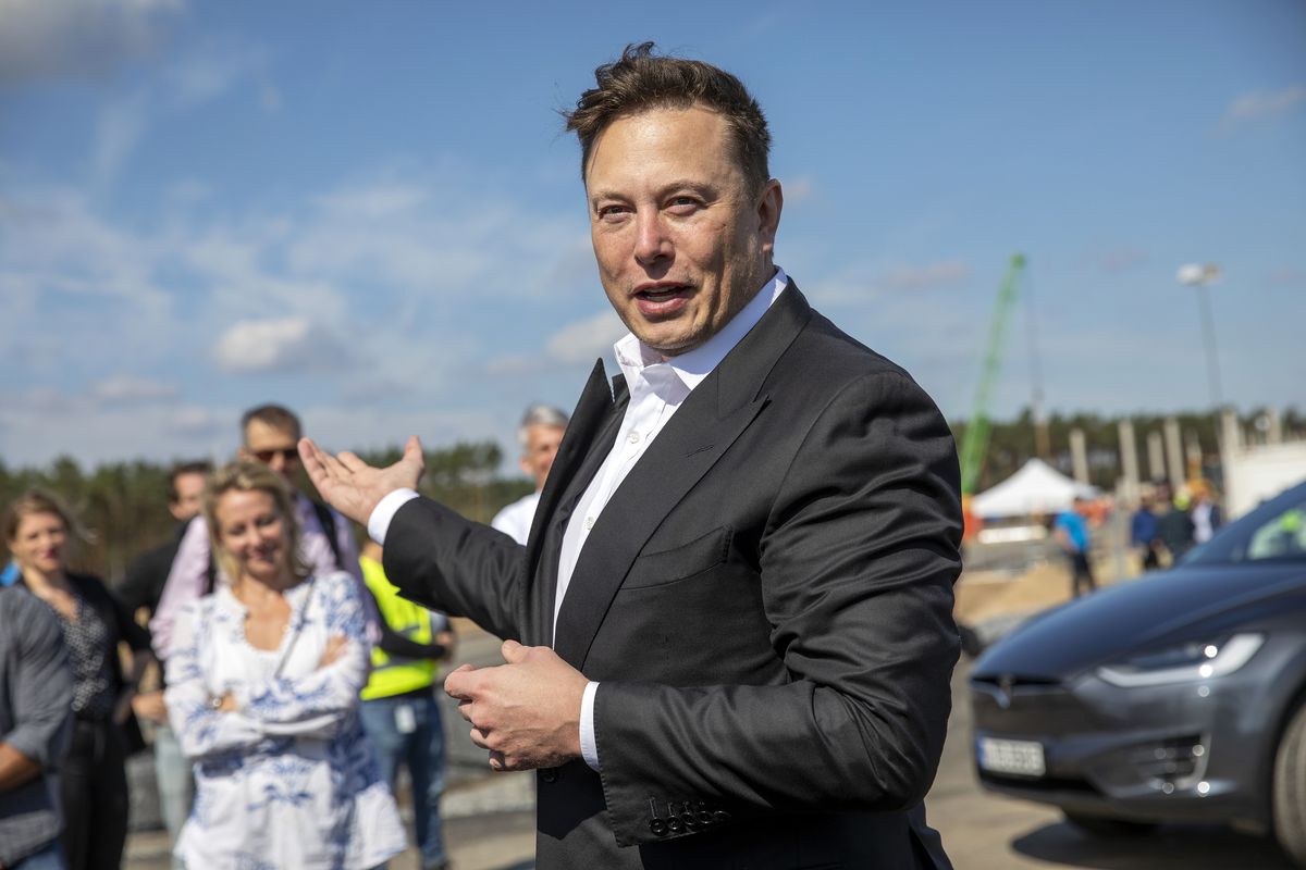 Elon Musk outdoors at a construction site speaking to members of the press.