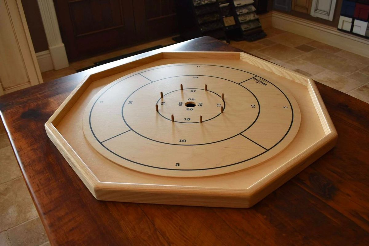 A Crokinole board photographed in uneven lighting on a dining table.