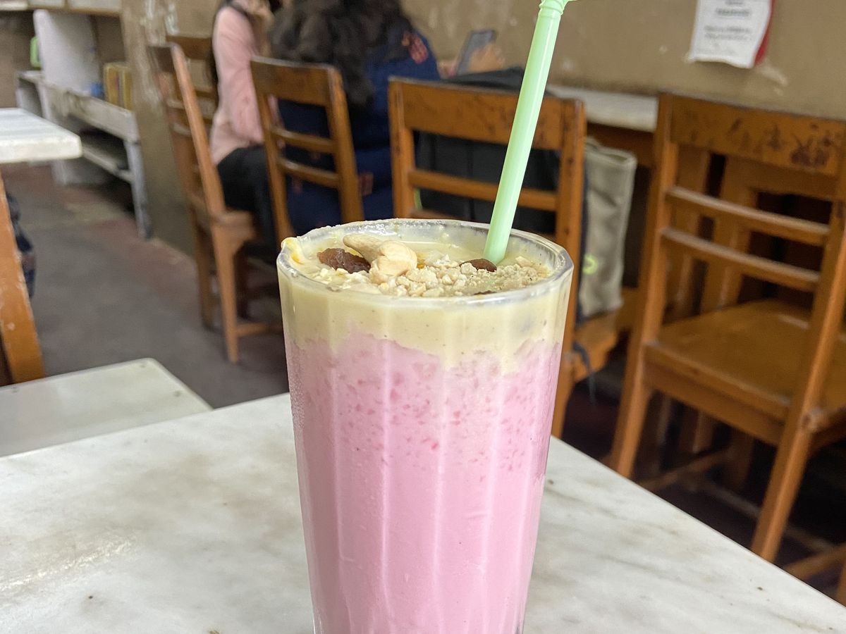 A bright pink beverage served in a sundae glass, topped with nuts and cream.