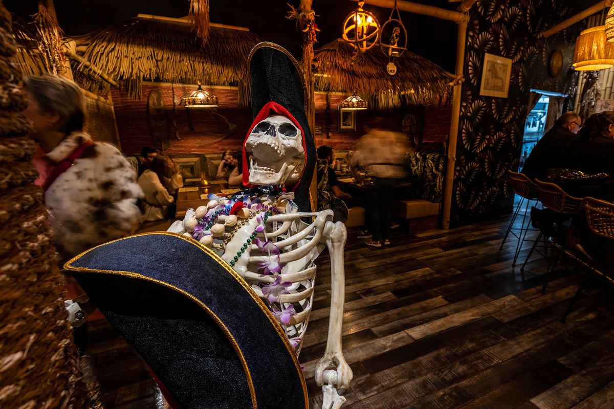 A plastic skeleton with open jaw inside a tiki restaurant.