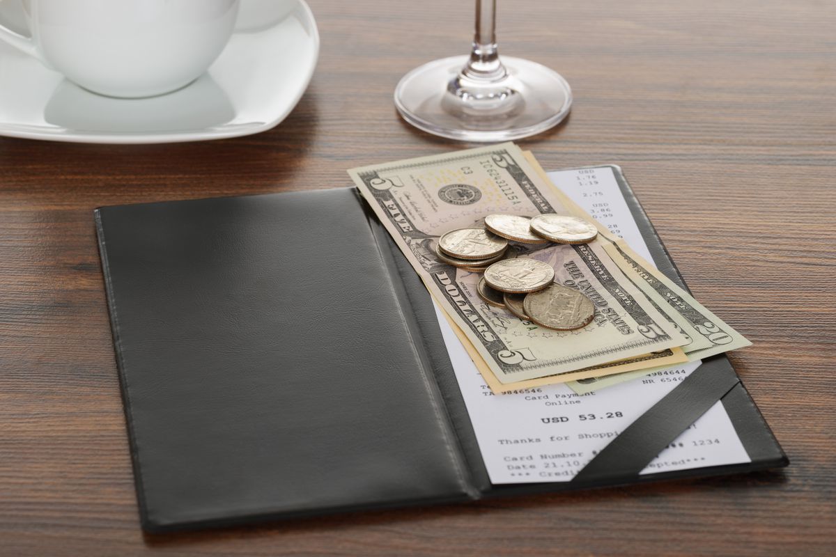 A restaurant bill on the table shows a receipt with a cash payment placed over top.