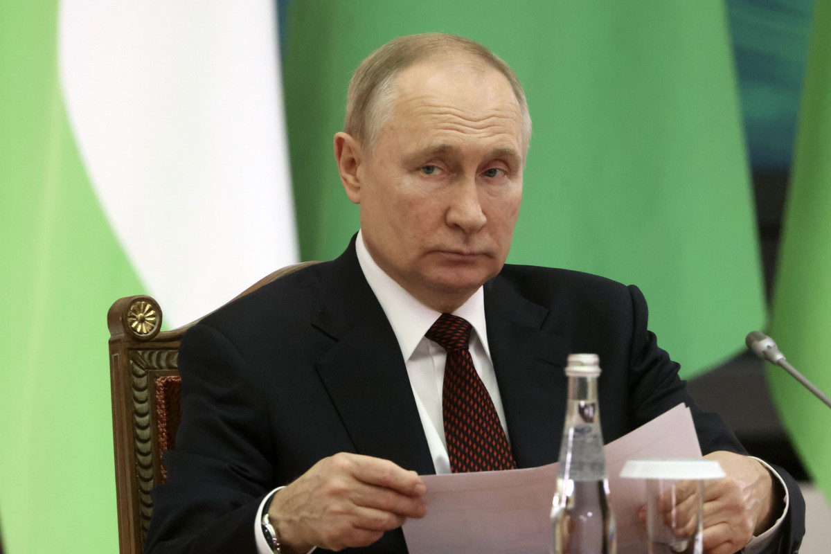 Russian President Vladimir Putin sitting at a table holding papers and not smiling.