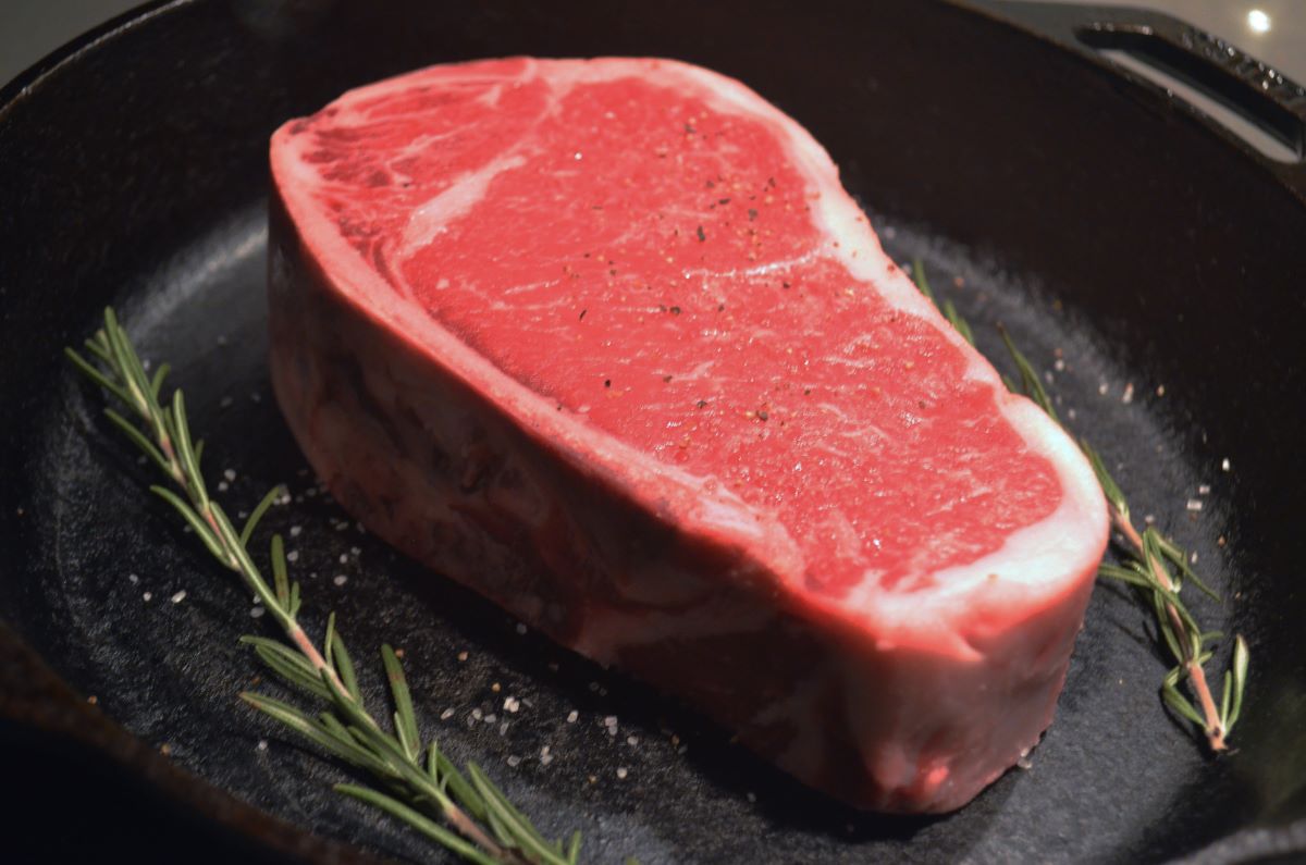 A steak is placed in a cast iron skillet with a few strands of rosemary on either side