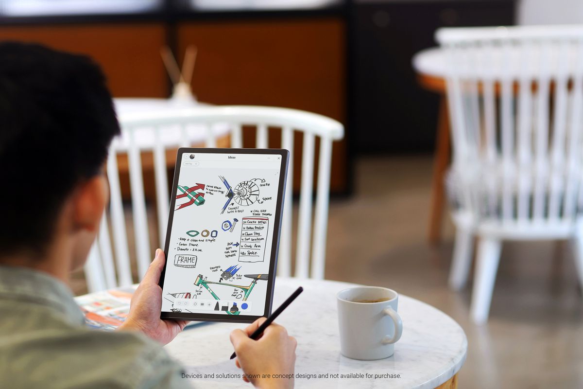 A worker holds the Dell Concept Stanza in their left hand in portrait mode at a white marble table in a cafe setting. On the screen are some drawings and notes. In their right hand is a black stylus.