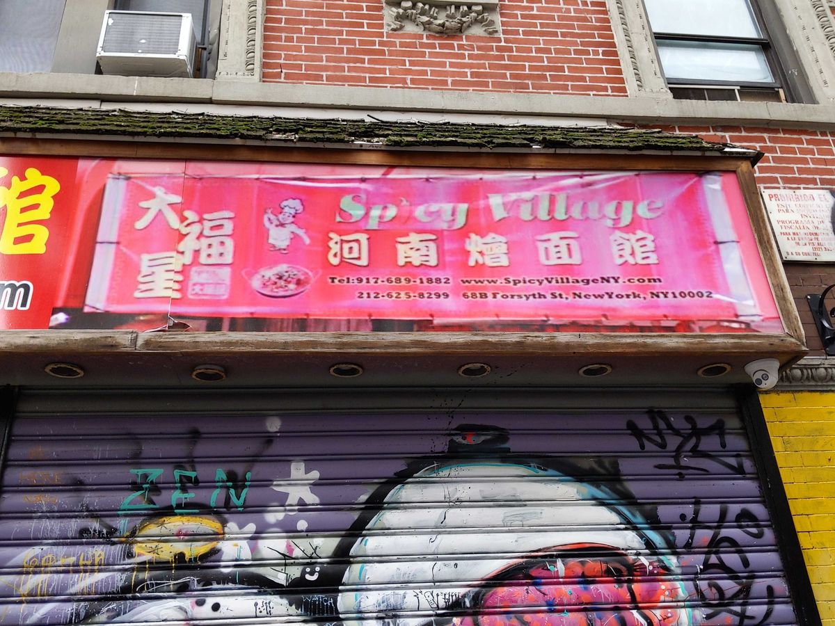 A pink banner reading Spicy Village hangs above a restaurant.