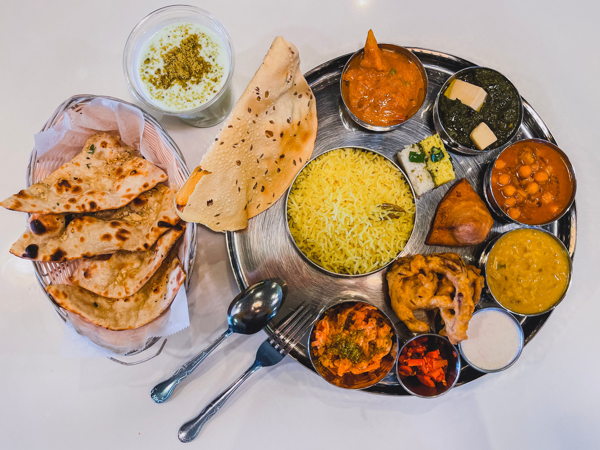 An overhead shot of a thali combination steel tray with a variety of Indian foods.