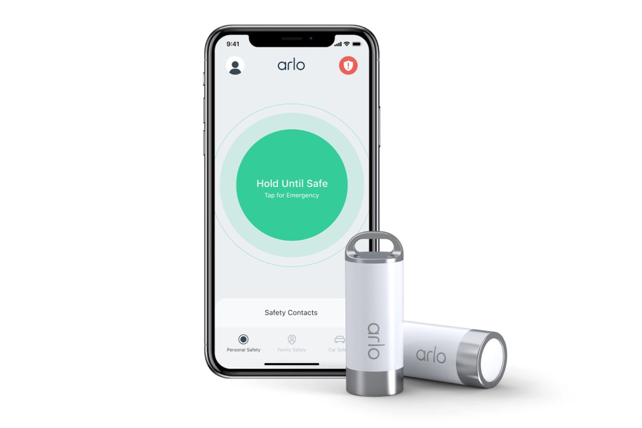 An iPhone X-series device is running Arlo’s new Safe app and is displaying a big green button that says “hold until safe” and “tap for emergency.” Alongside the phone are two of Arlo’s new safe buttons that are white and silver cylinders that look like batteries, have a button on one end and a built-in keychain loop on the other.