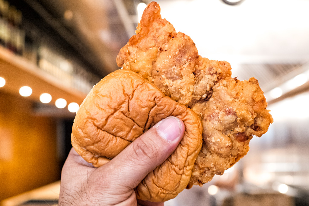 A hand holds up a fried chicken sandwich, a large crispy patty jutting out of a squishy bun