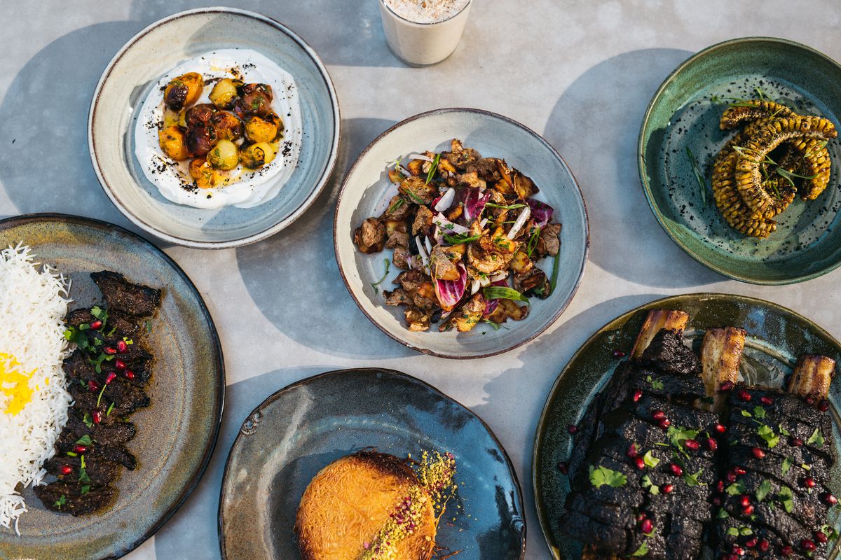 A spread of Persian dishes, including rice and kabobs, corn ribs, vegetables plated over a creamy dish, and more.