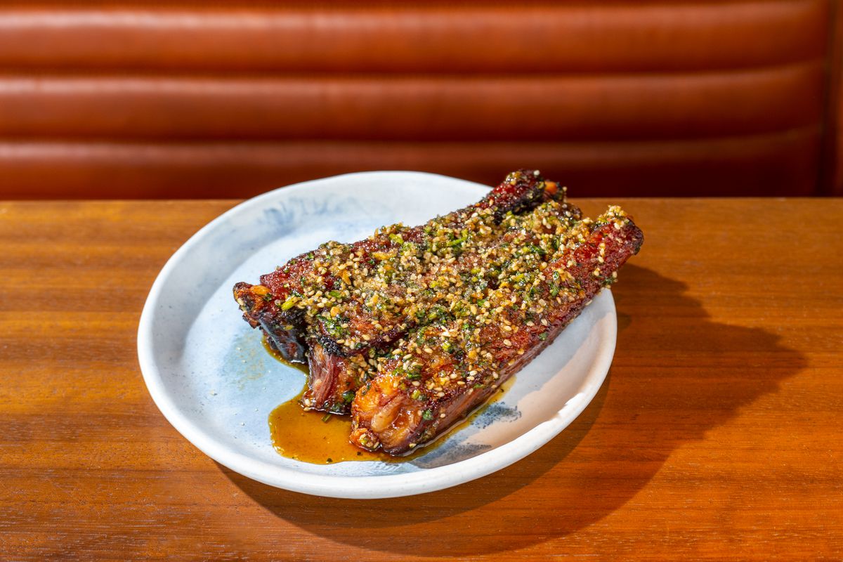 Sweet and sour ribs, garnished with green garlic and sesame seeds, sit on a plate