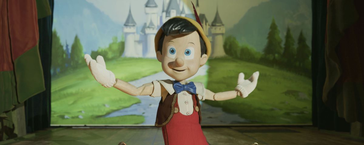 A CG version of the wooden puppet-boy Pinocchio kneels on a stage with his arms stretched wide in Disney’s 2022 live-action remake of its 1940 animated classic
