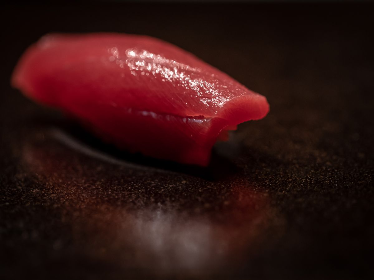 A crimson slice of lean tuna nigiri sushi sits on a black surface