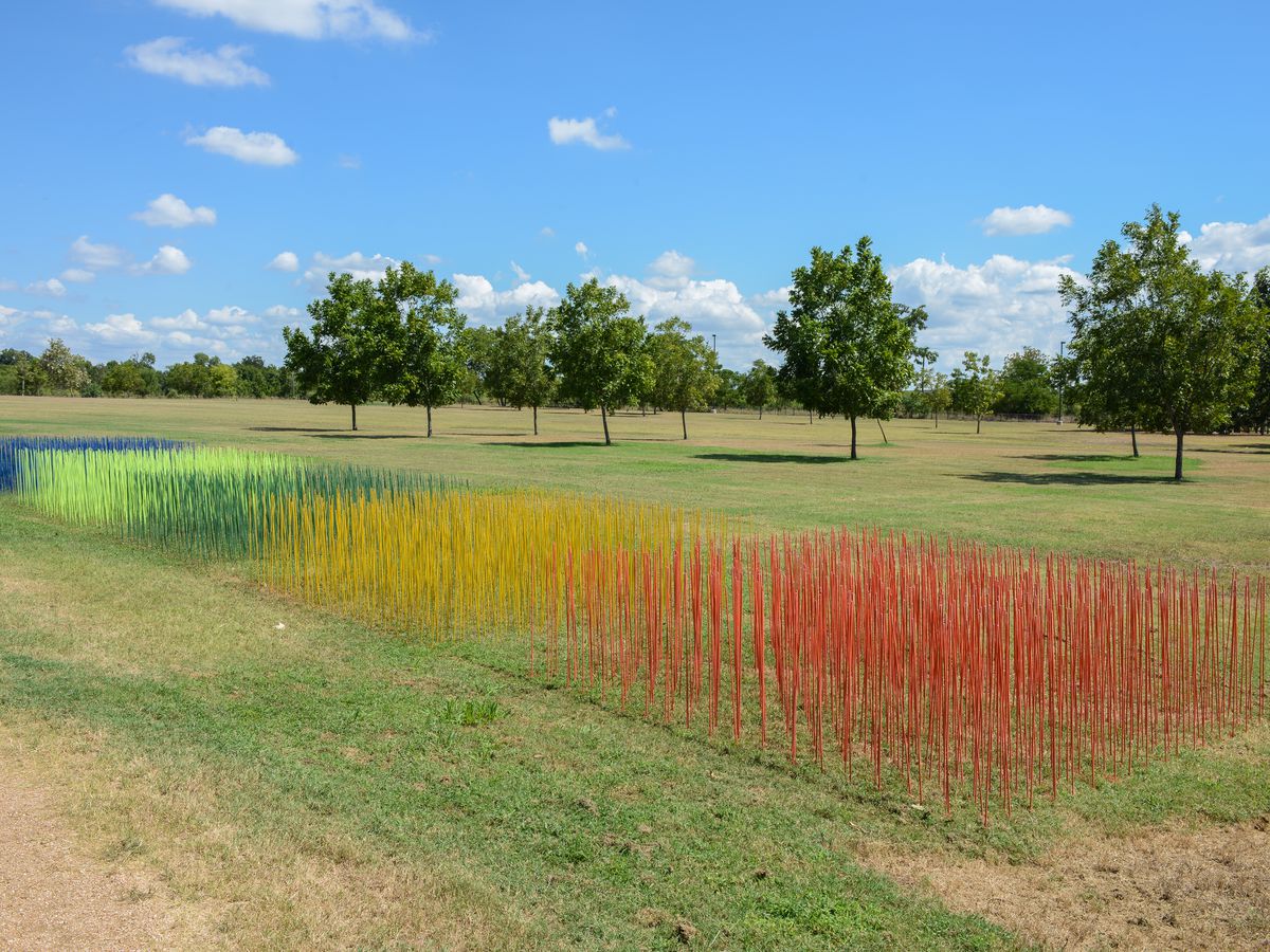 A work of art called Color Field by Augustina Rodriguez. Colorful rods are interspersed with the grass in a field.