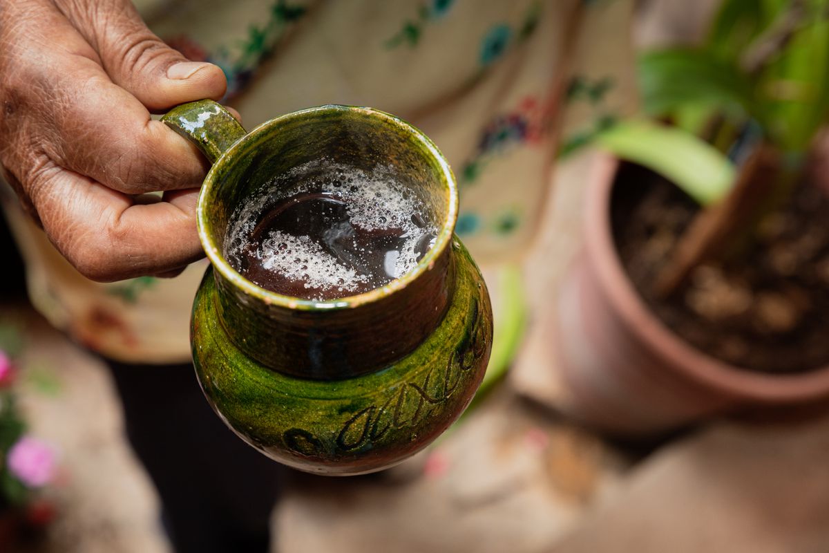 A green ceramic mug is being held by a weathered hand.