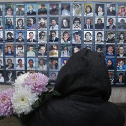 A woman with flowers stands in front of portraits of victims of a theatre siege  in Moscow, Russia, Friday, Oct. 26, 2012. Families the 130 people who died in a hostage crisis at a Moscow theater 10 years ago will hold a ceremony outside the venue where Chechen militants held 912 audience members for three days. 