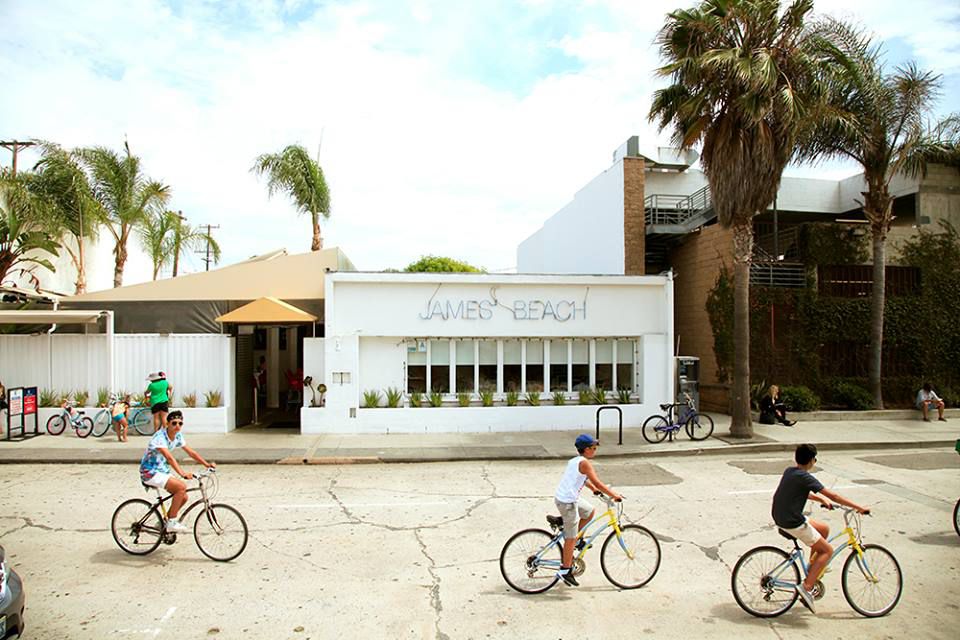 Three bike riders pass in front of a white restaurant building.
