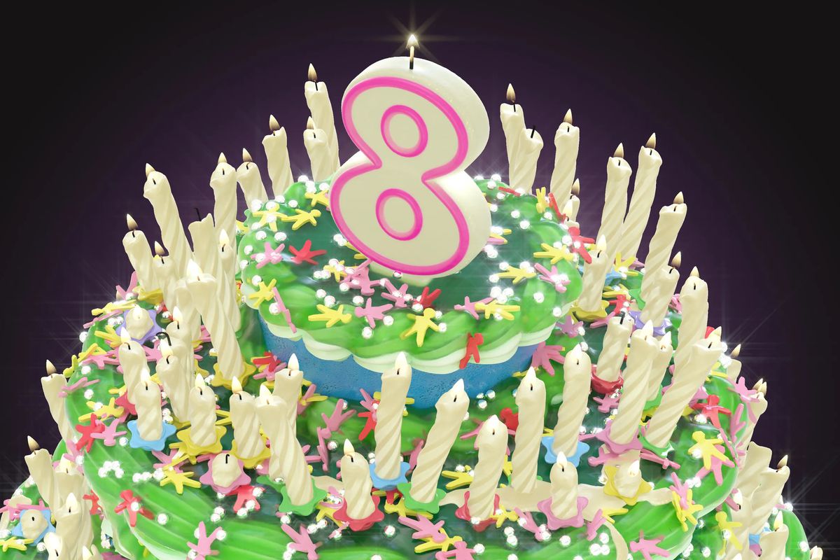 A large three-tiered, white-frosted birthday cake with green piping on the edges, a ring of many small candles, and a large candle shaped like the number 8 on top.