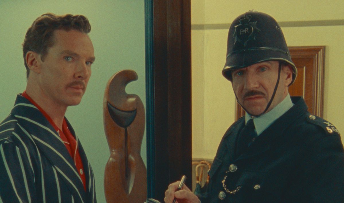 Benedict Cumberbatch (as Henry Sugar) and Ralph Finnes (dressed as a policeman) look directly into the camera in a scene from Wes Anderson’s Netflix film The Wonderful Story of Henry Sugar