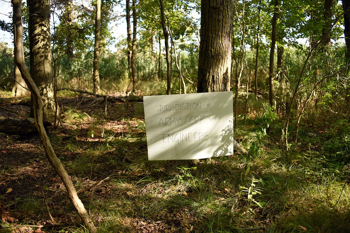 A clearing in a forest with several large trees. A sign that says “Jurisdiction of Army Corps of Engineers” sits in the clearing. 