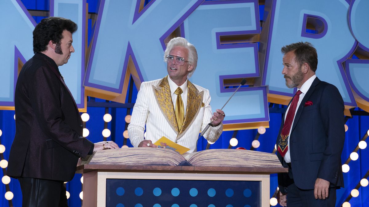 Danny McBride and Stephen Dorff stand on opposite sides of a lectern, where Walton Goggins runs a game show as Baby Billy in The Righteous Gemstones.