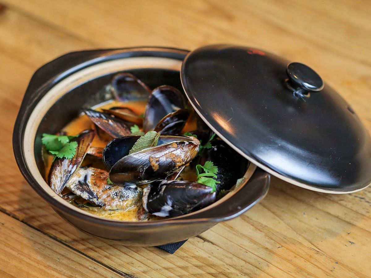 A sleek gray dish with a cover tilted off to reveal enticing-looking mussels 