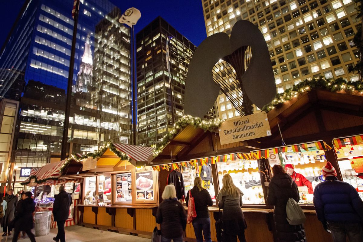 Visitors line up in front of a row of brightly-lit booths with lit-up skyscrapers in the background