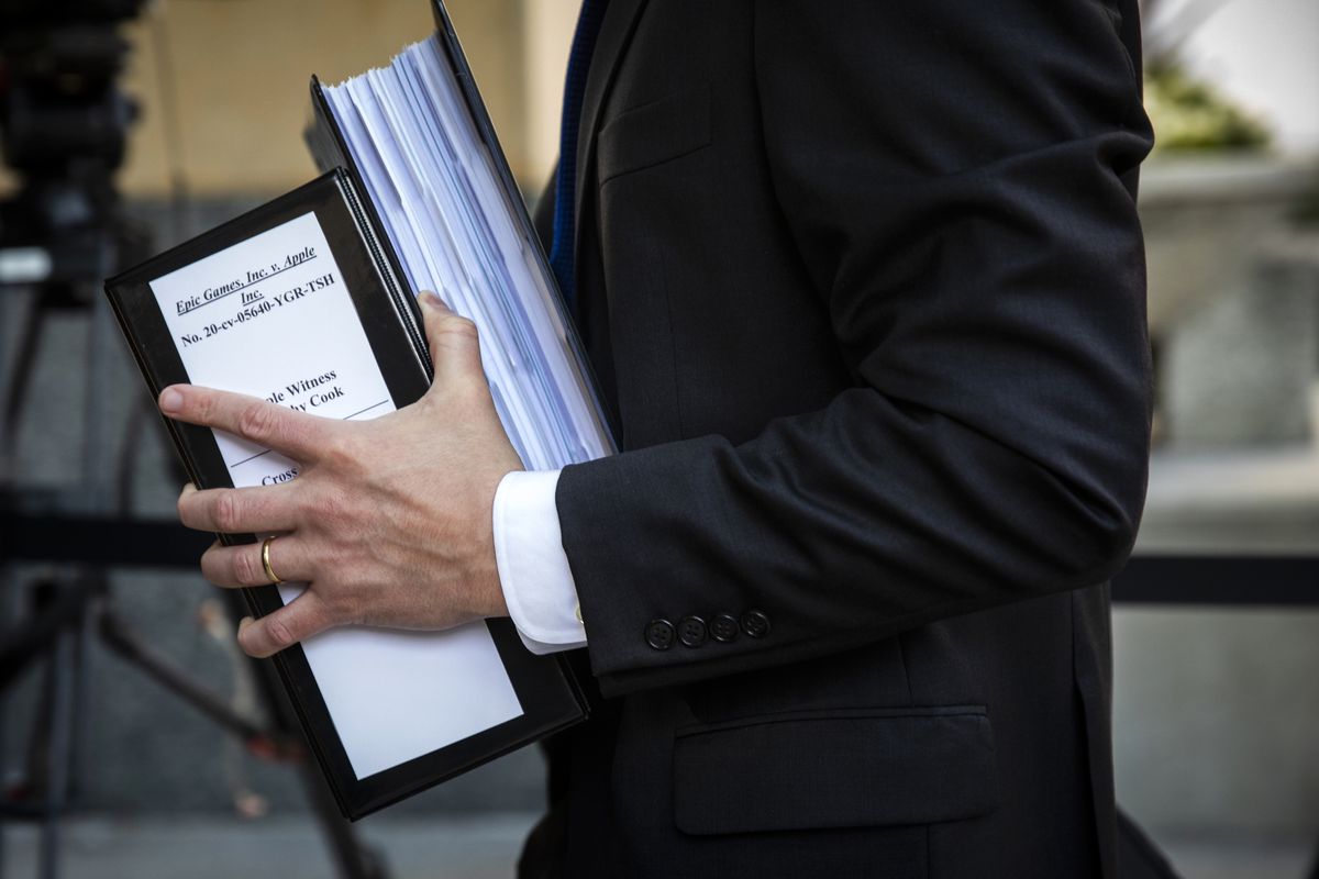 A person in a dark suit carries two large binders full of papers.