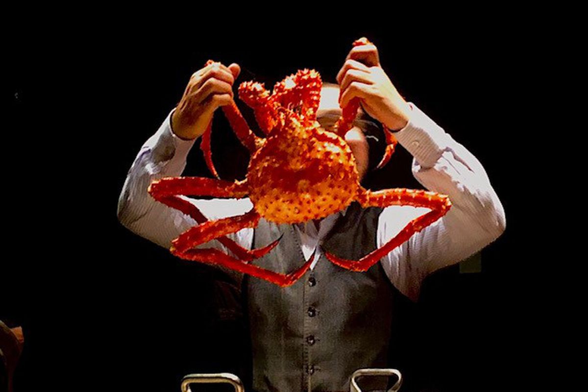 A chef holds up a king crab by the claws over a metal pan.