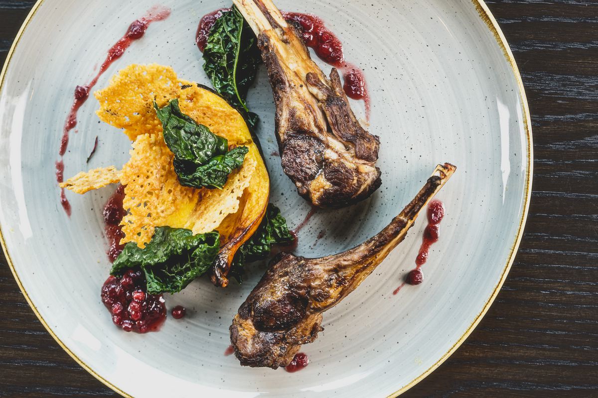 Legs of roasted lamb on a plate with bright swirls of puree, roasted squash, and greens