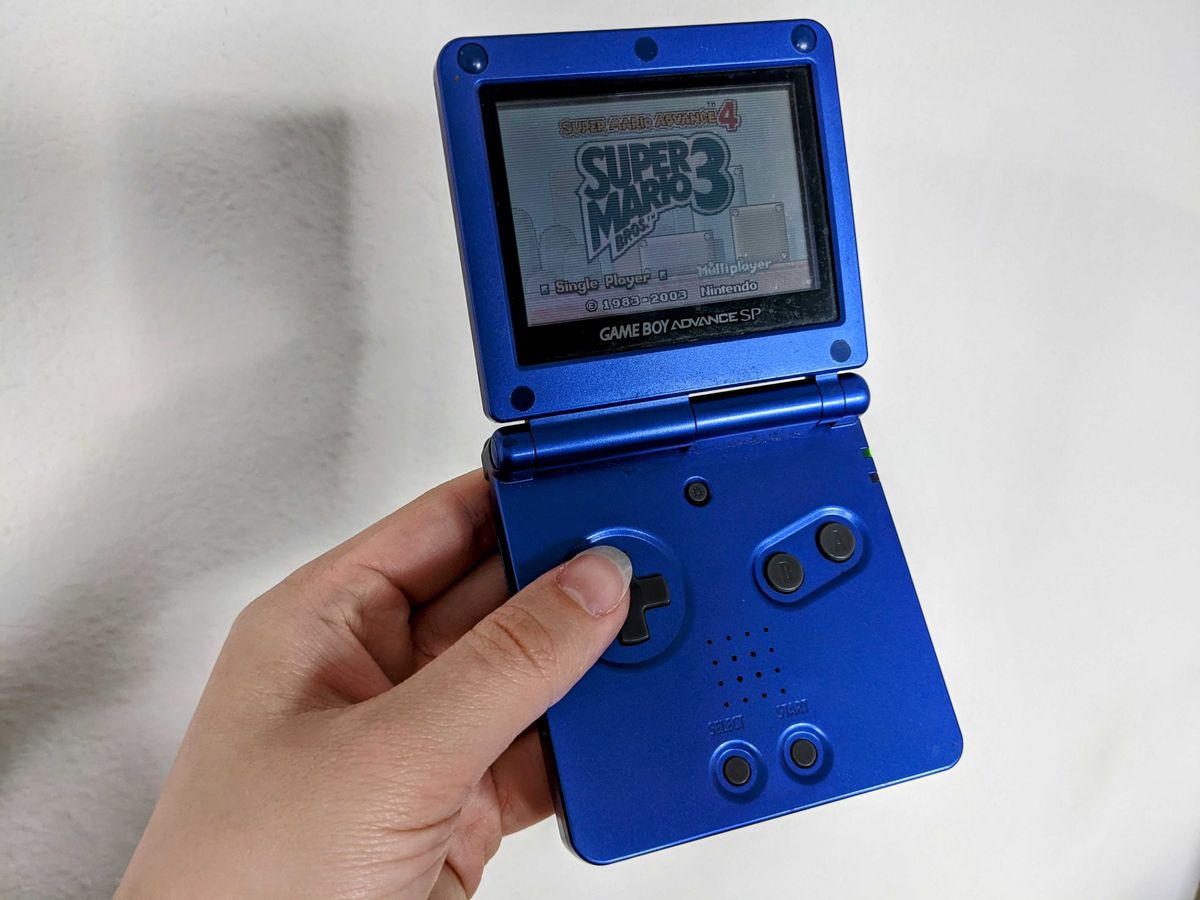 A hand holding up a purple Game Boy Advance SP with Super Mario Bros. 3 faintly visible on the screen.