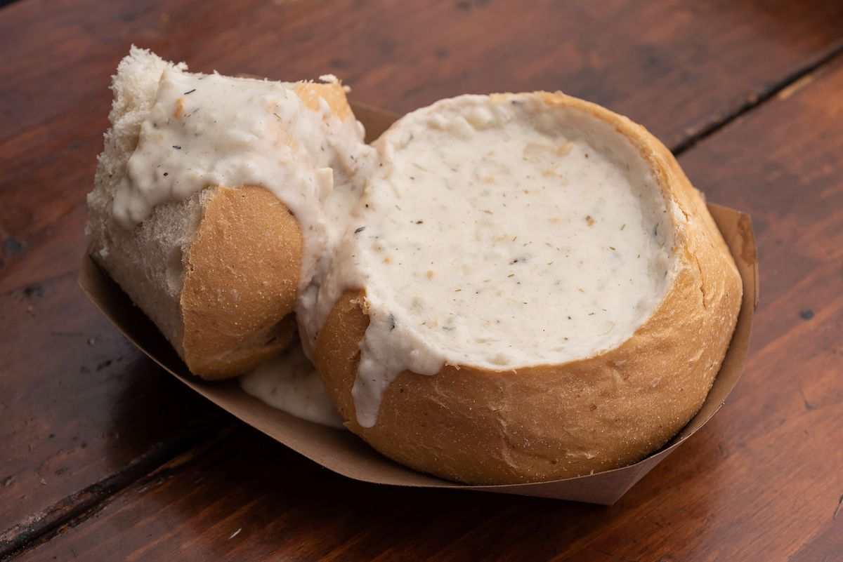 Clam chowder in a bread bowl on a wooden table.